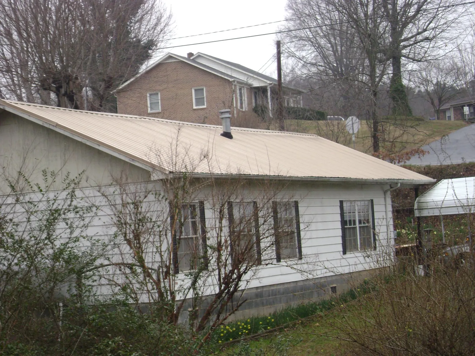 Tan metal roof on a white sided house set into a hillside — Commercial Roofing by Roofing Brothers in Belvedere Tiburon